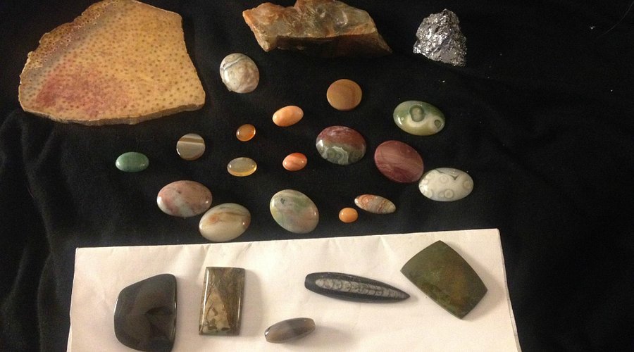 Various polished and unpolished stones and minerals displayed on a black surface and a white sheet.